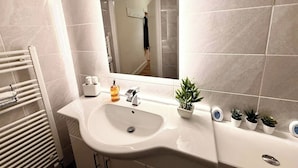 Ein Badezimmer mit einem weißen Waschbecken, einem Spiegel, einem Handtuchhalter und einer Topfpflanze.