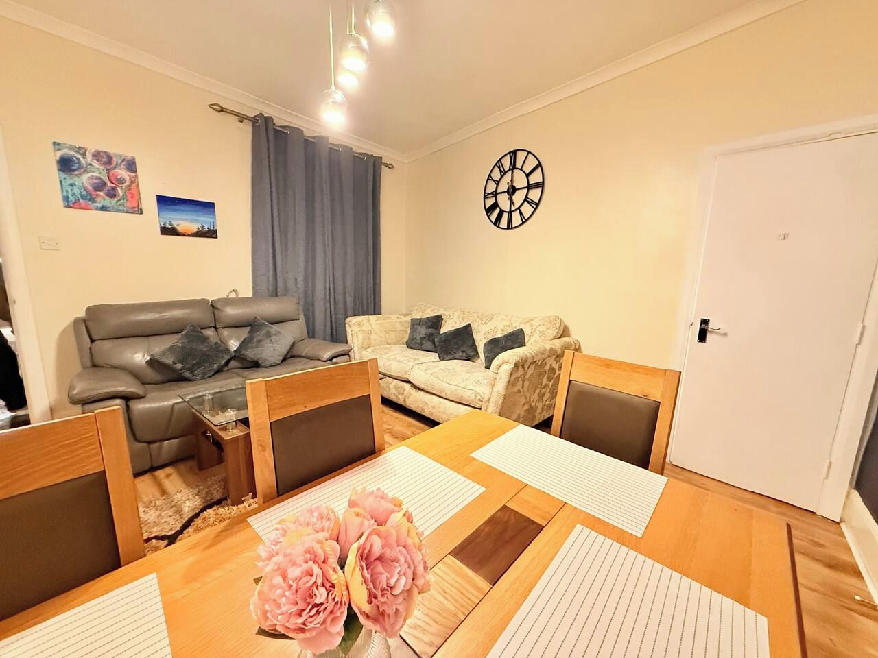 Un salon avec un canapé, une table à manger et des chaises, une horloge au mur et une porte.