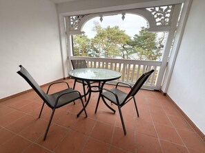 A balcony with a round table and four chairs, a white railing, and a view of trees. - Villa Seeadler 615 (Binz)