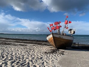 A boat with multiple red flags on a sandy beach with a body of water in the background. - Villa Seeadler 615 (Binz)