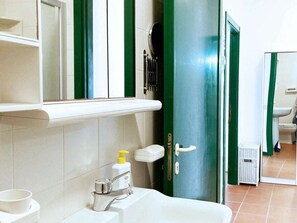 Ein Badezimmer mit weißem Waschbecken, einem Spiegel, einer grünen Tür und einer durch die Tür sichtbaren Toilette.