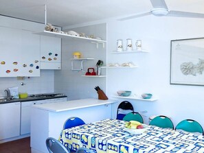 Eine kleine Küche mit weißen Schränken, einem Gasherd und einem Essbereich mit Tisch und Stühlen.