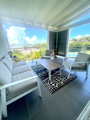 A modern outdoor seating area with a view of a pool and landscape. - Petite Maison Duplex Cosy • Piscine • Près de Pinel (Cul-de-Sac)