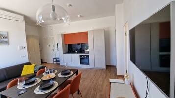 Eine moderne Küche mit orangenen Schränken, ein Essbereich mit Tisch für zwei Personen und ein großer Fernseher an der Wand.