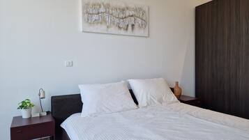 Ein Schlafzimmer mit einem Bett, einem Nachttisch, einem Wandbild und einem dunkel gefärbten Kopfteil.