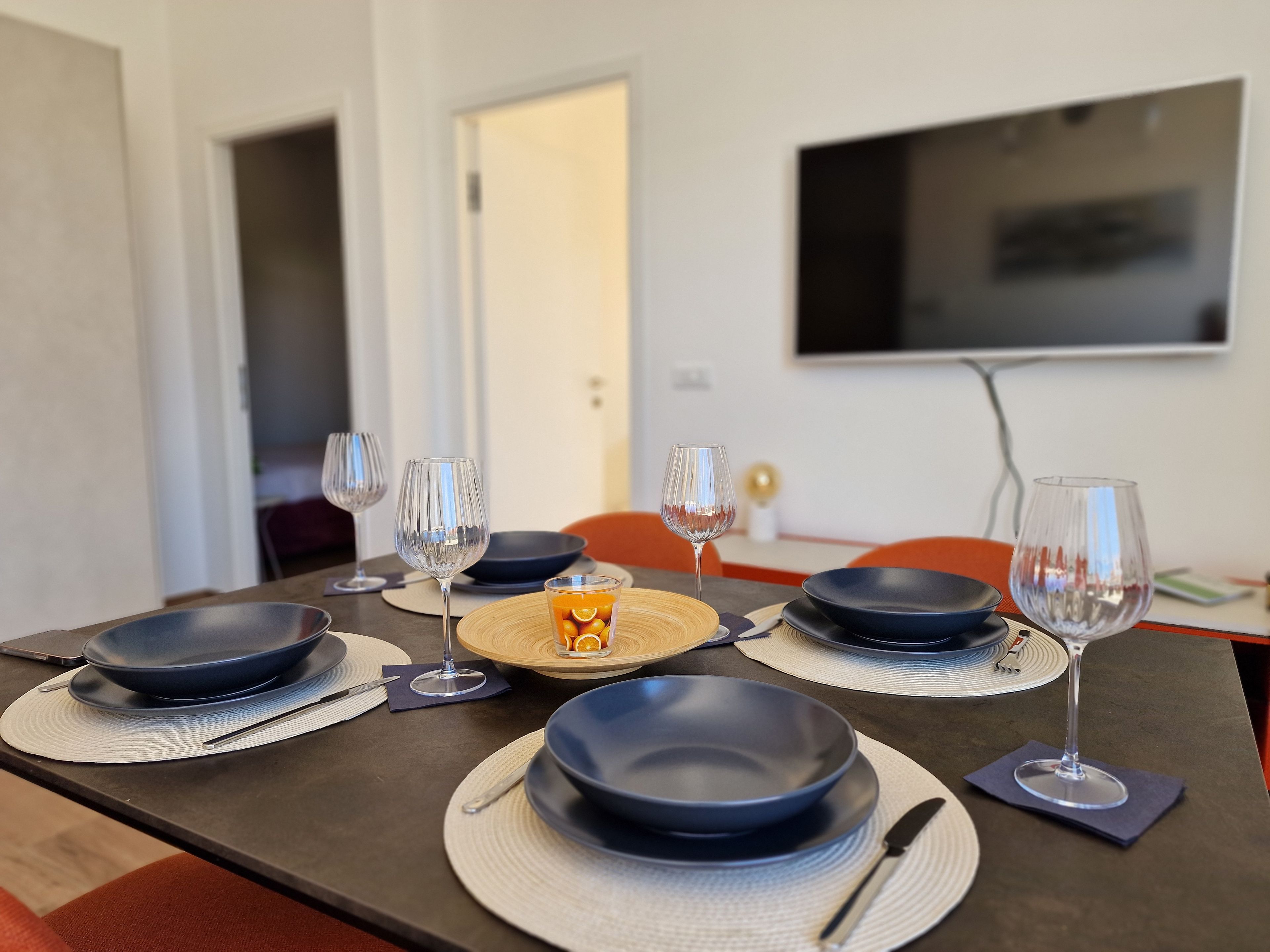 Een eettafel gedekt met borden, glazen en bestek, met een televisie die aan de muur hangt op de achtergrond.