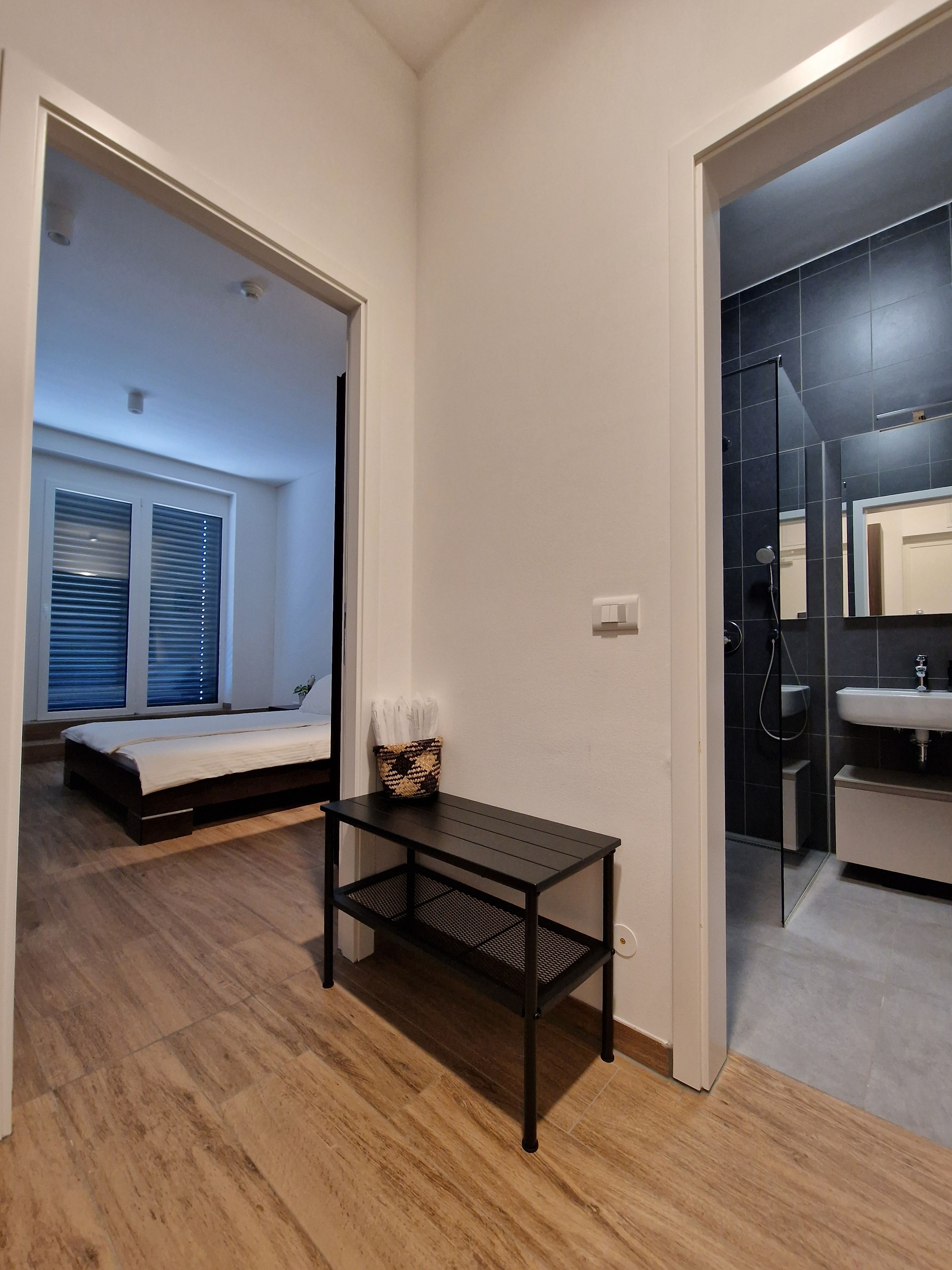 A bedroom with a bed, a small table, and a window with blinds.