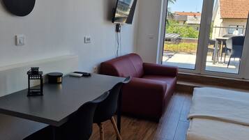 Ein modernes Zimmer mit einem Bett, einem Schreibtisch mit Stühlen, einem Fernseher und Blick ins Freie.