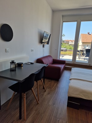 A modern room with a bed, a desk with chairs, a television, and a view of the outside.