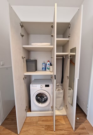 A compact laundry room with a washing machine, shelves, and a drying rack.