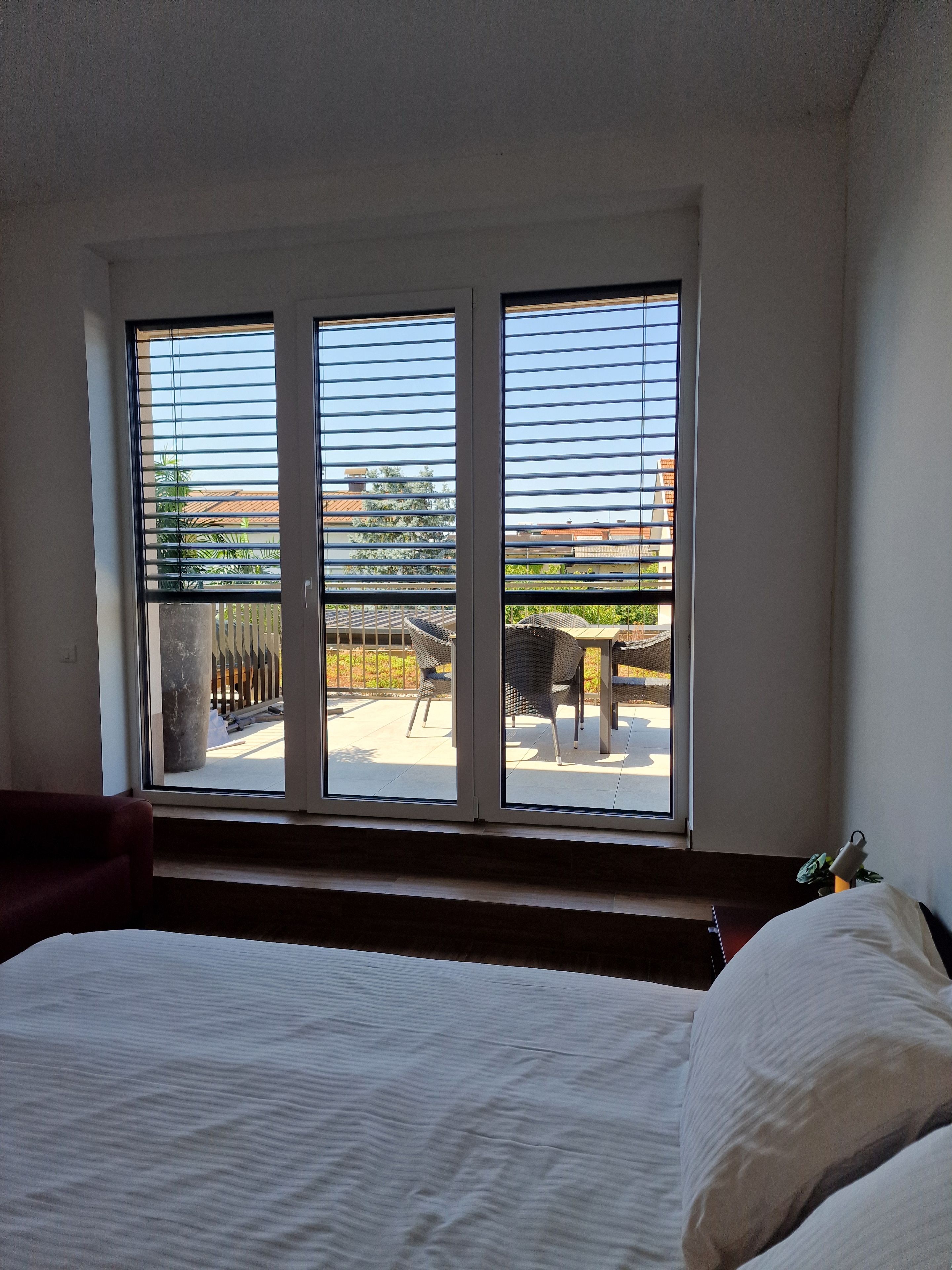 Een kamer met een bed, een raam met zonwering en uitzicht op het omliggende landschap.