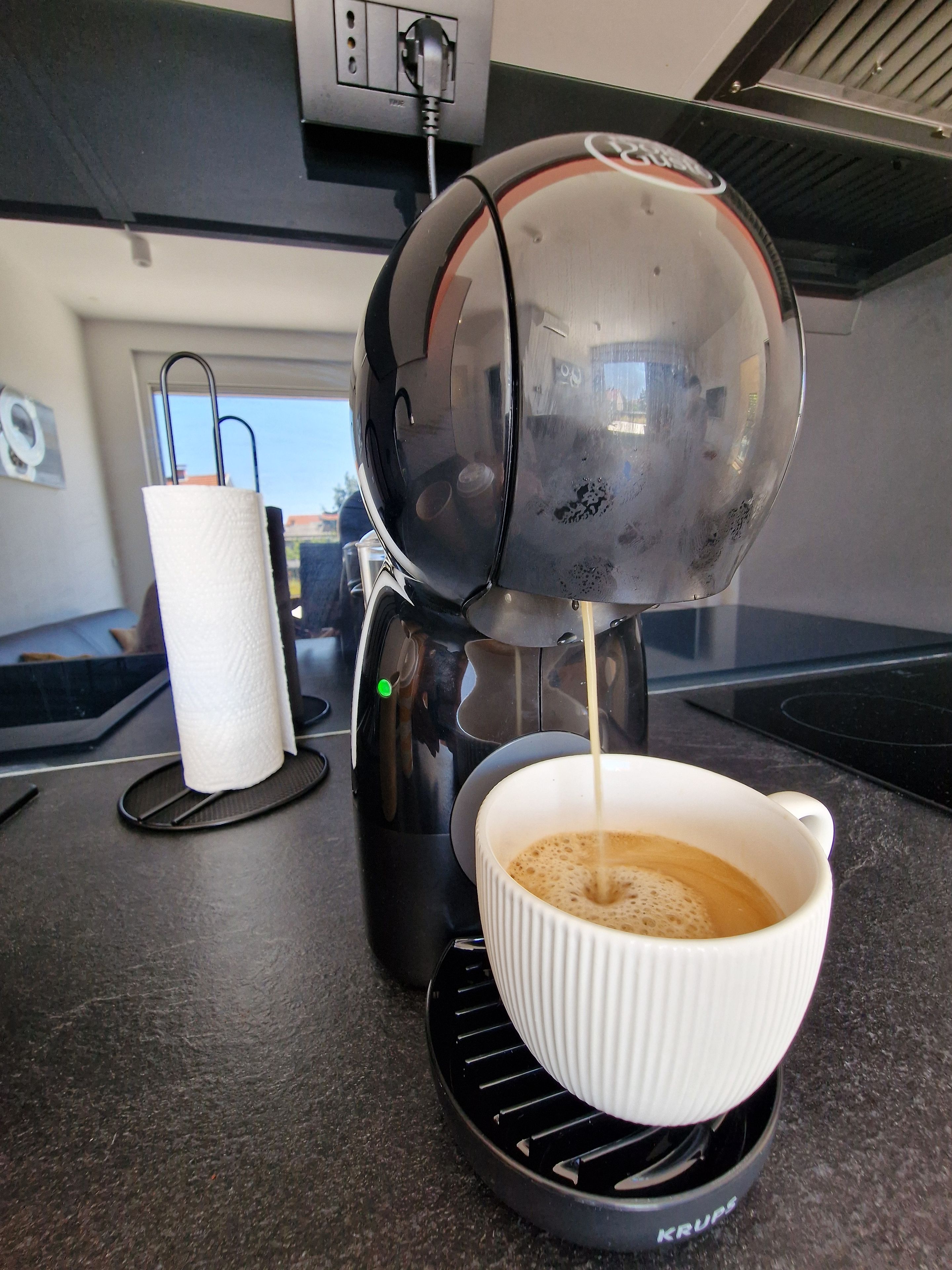 En kaffemaskine serverer kaffe i en hvid kop på en sort underkop.