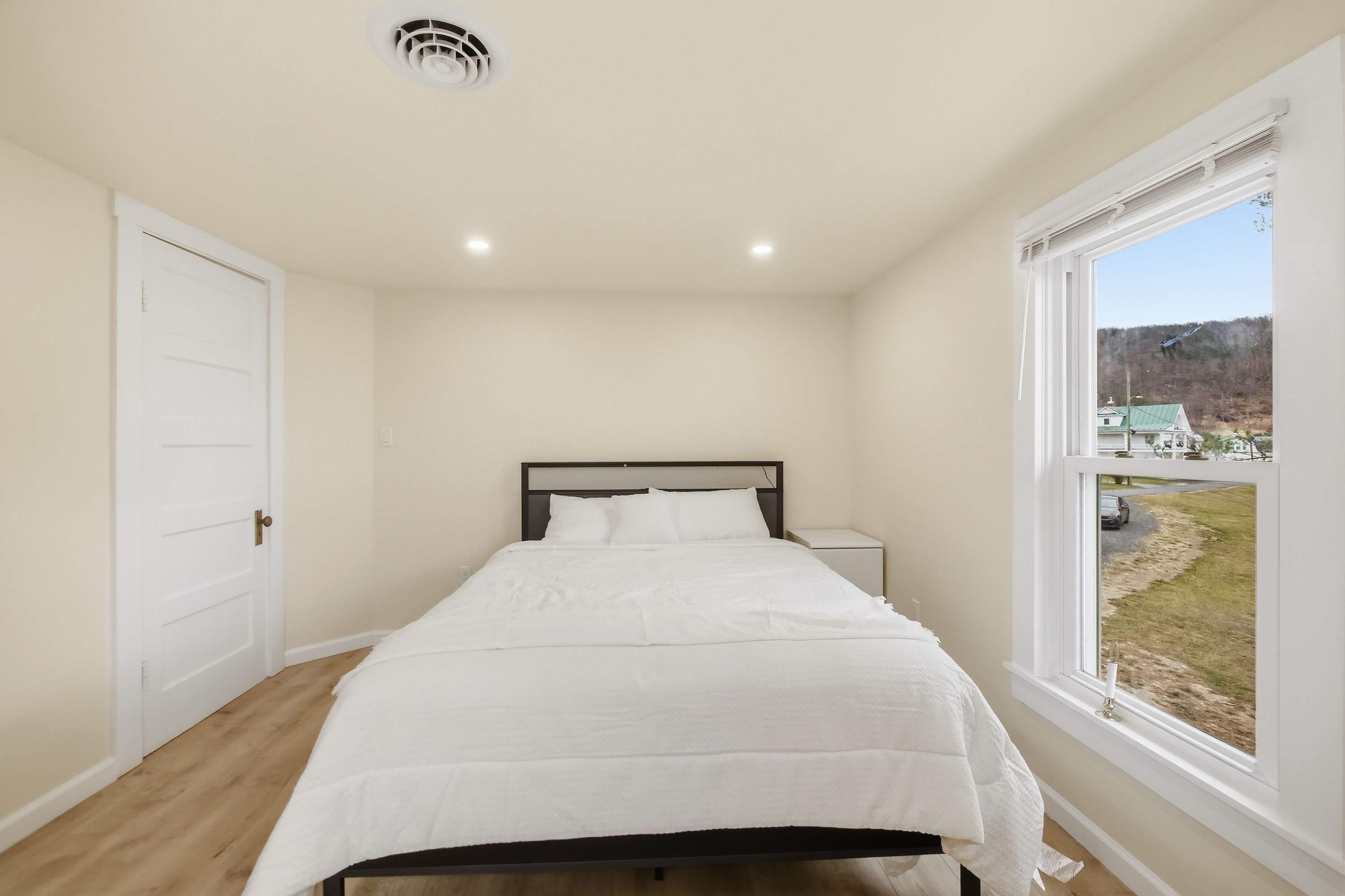 Un dormitorio con cama, mesita de noche, ventana con vistas y puerta.
