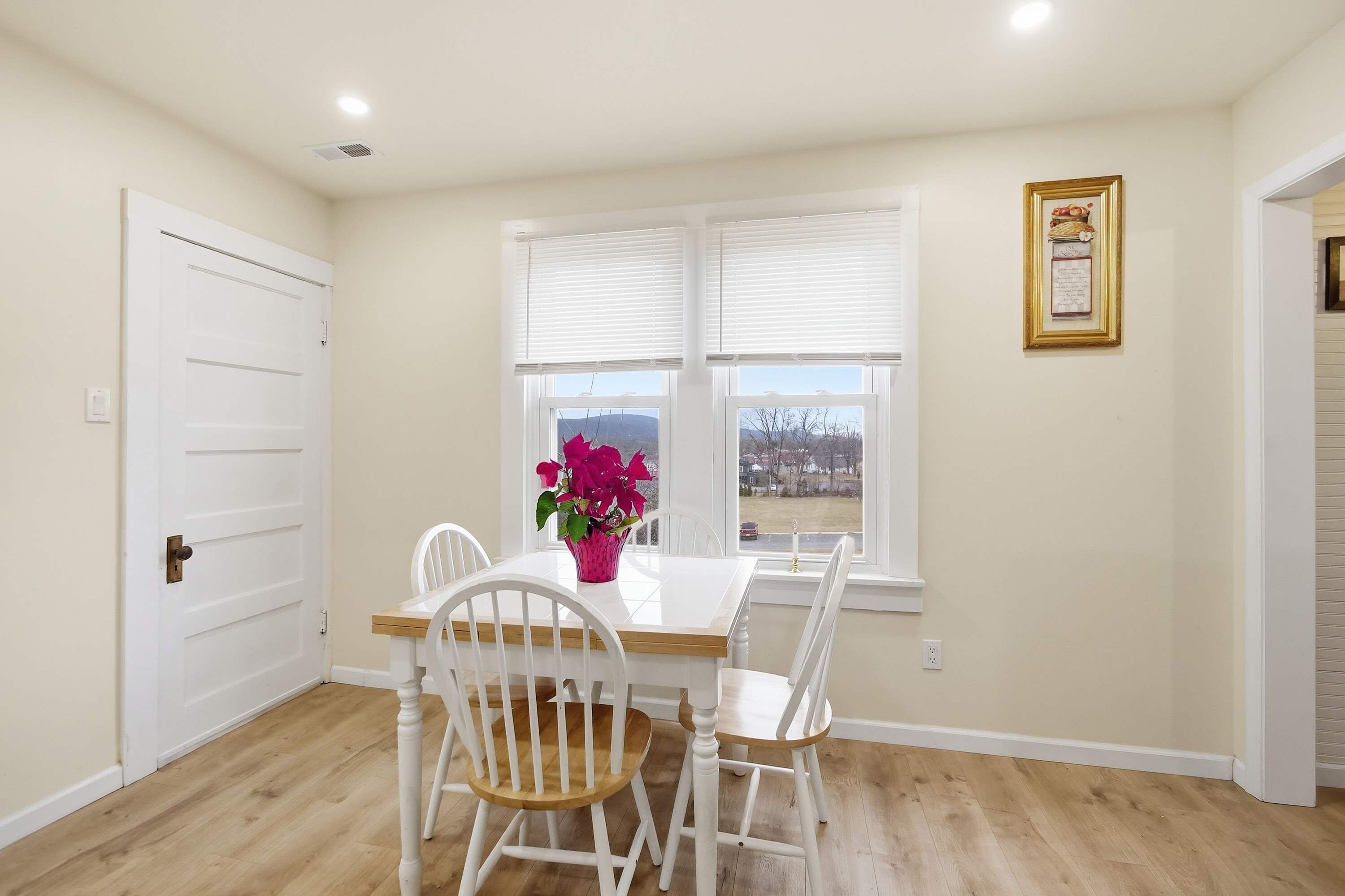 Un comedor con una mesa y sillas blancas, una ventana con persianas y un certificado enmarcado en la pared.