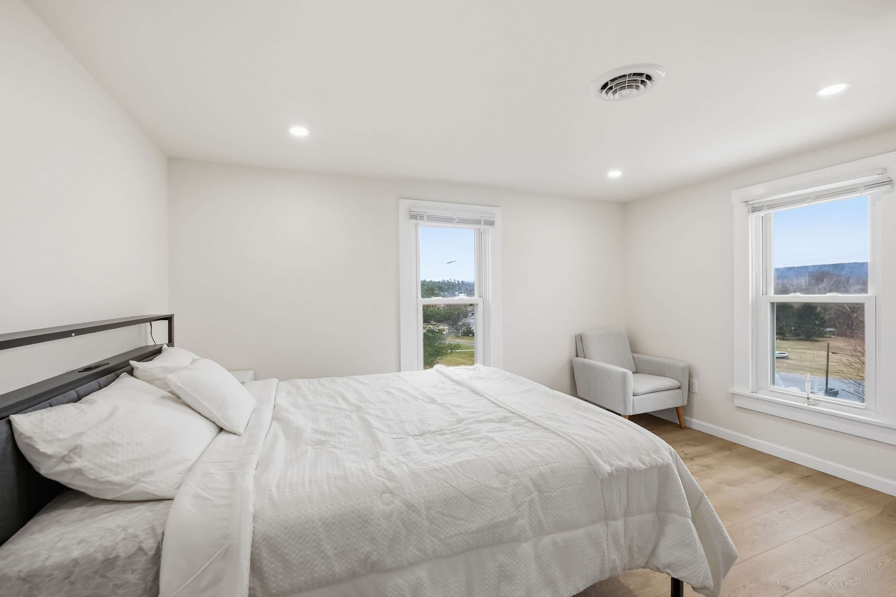 Un dormitorio con una cama, una silla y ventanas amplias.