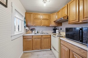 Una cocina con armarios de madera, un lavamanos de acero inoxidable, una estufa y un microondas Kenmore.
