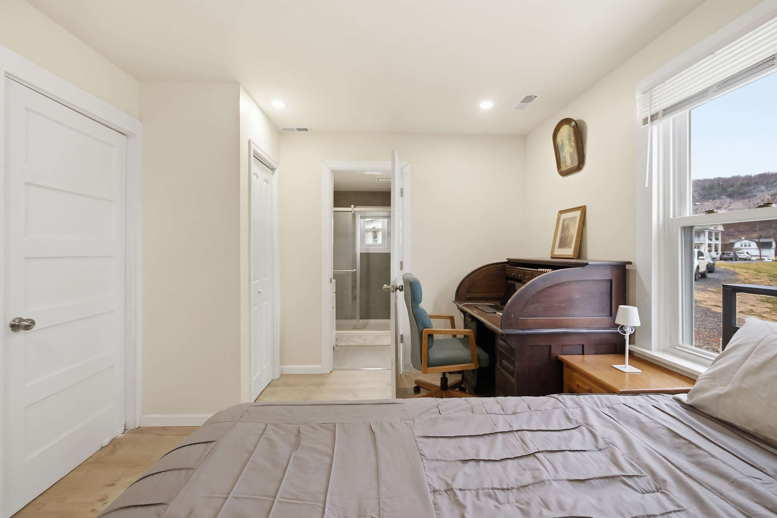 Une chambre à coucher avec un lit, un bureau, une chaise, une fenêtre et une porte.