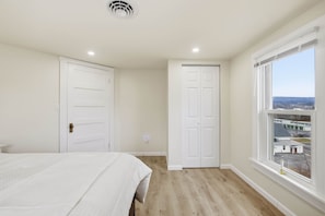 A bedroom with a bed, two white doors, a window with a view, and a ceiling vent. - Historic Wardensville Home w Mountain Views (Wardensville)