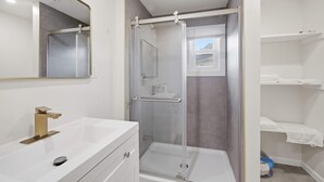 Casa de banho com lavatório branco, espelho, cabine de duche e porta-toalhas.