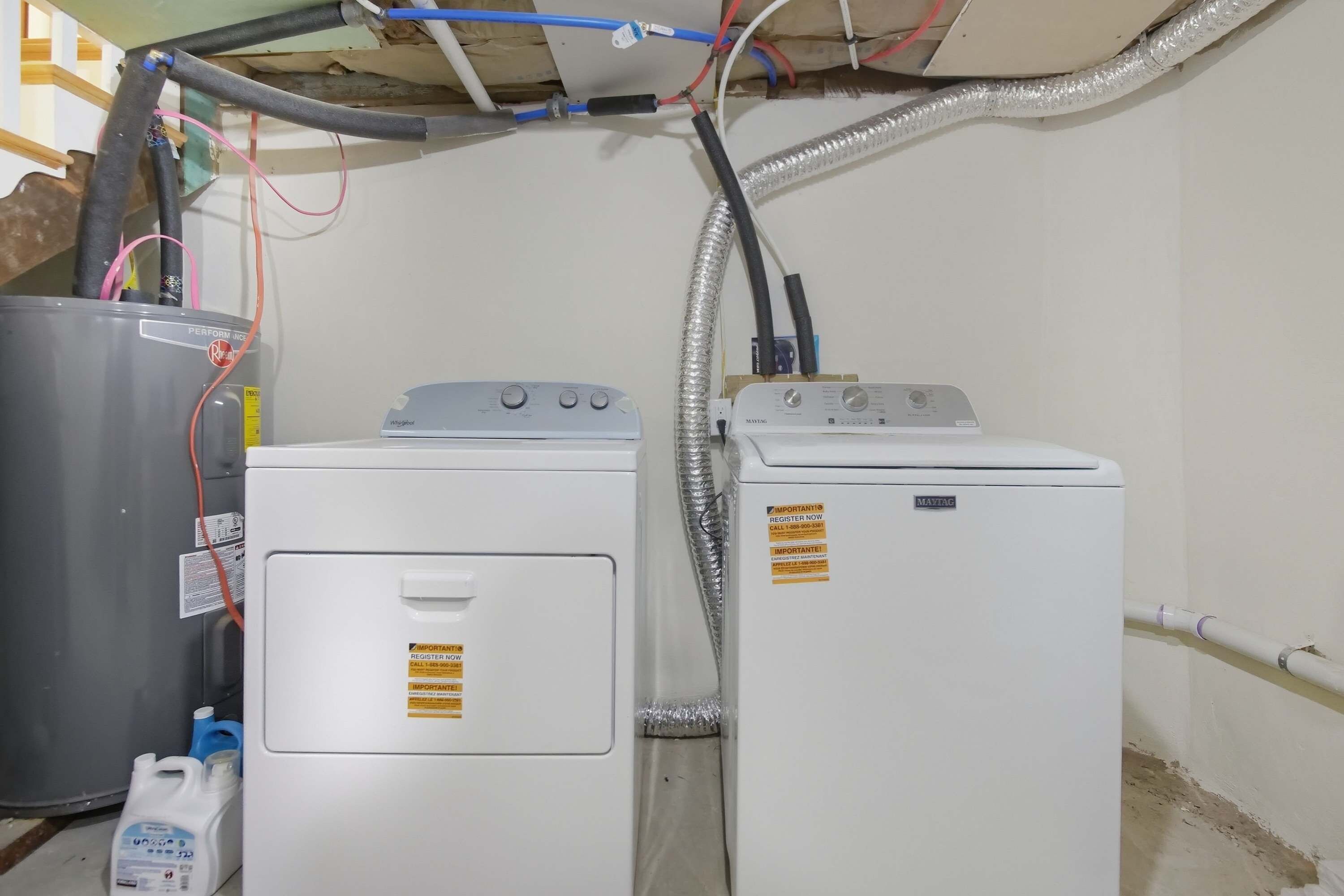 Une buanderie équipée de deux machines à laver et d’un grand récipient en métal, reliés par une tuyauterie visible.