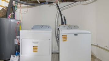 Une buanderie équipée de deux machines à laver et d’un grand récipient en métal, reliés par une tuyauterie visible.