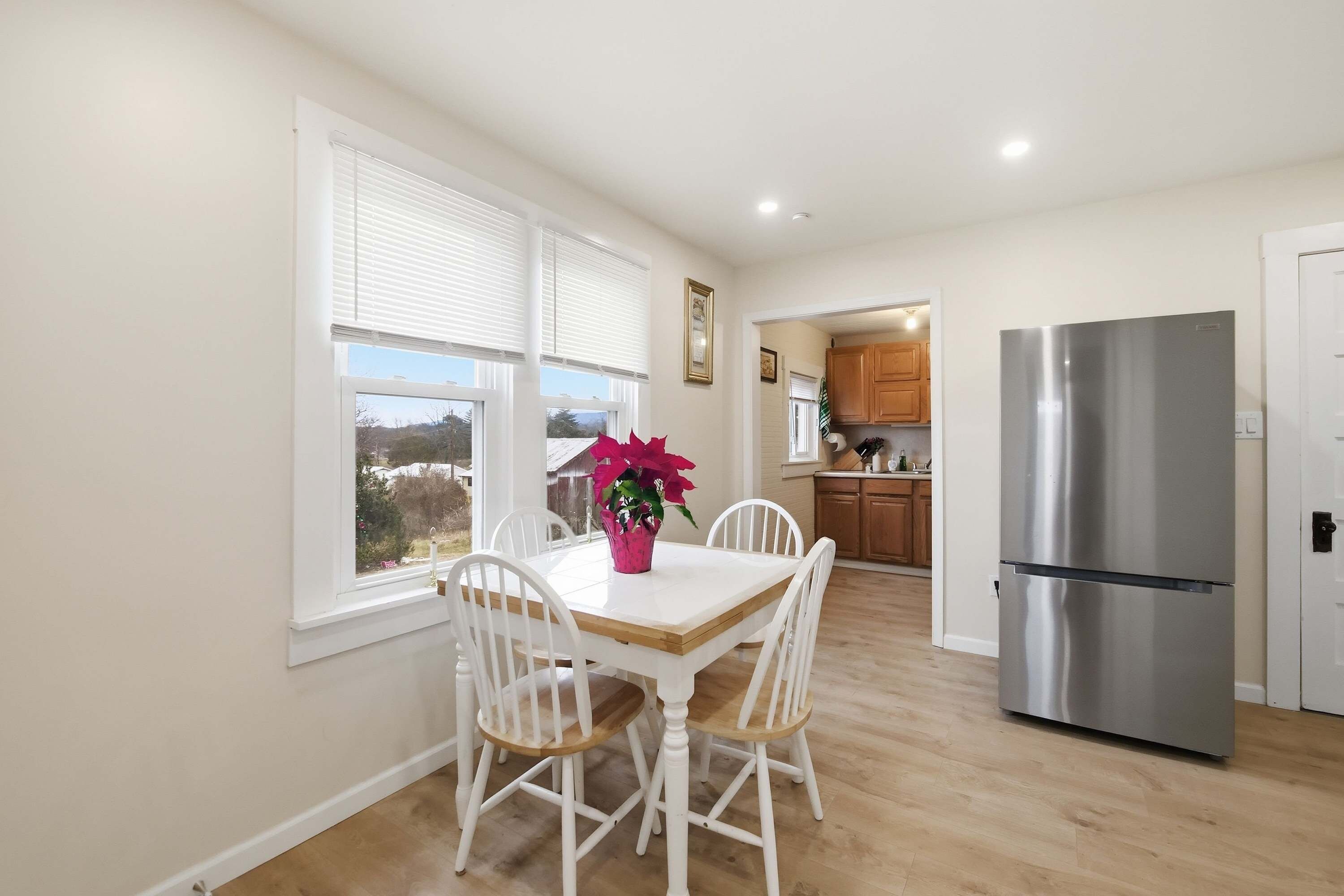 Una cocina con refrigerador de acero inoxidable, armarios blancos y una mesa de comedor con sillas blancas.