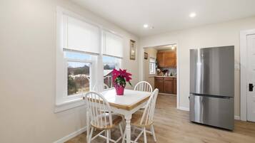 Una cocina con refrigerador de acero inoxidable, armarios blancos y una mesa de comedor con sillas blancas.