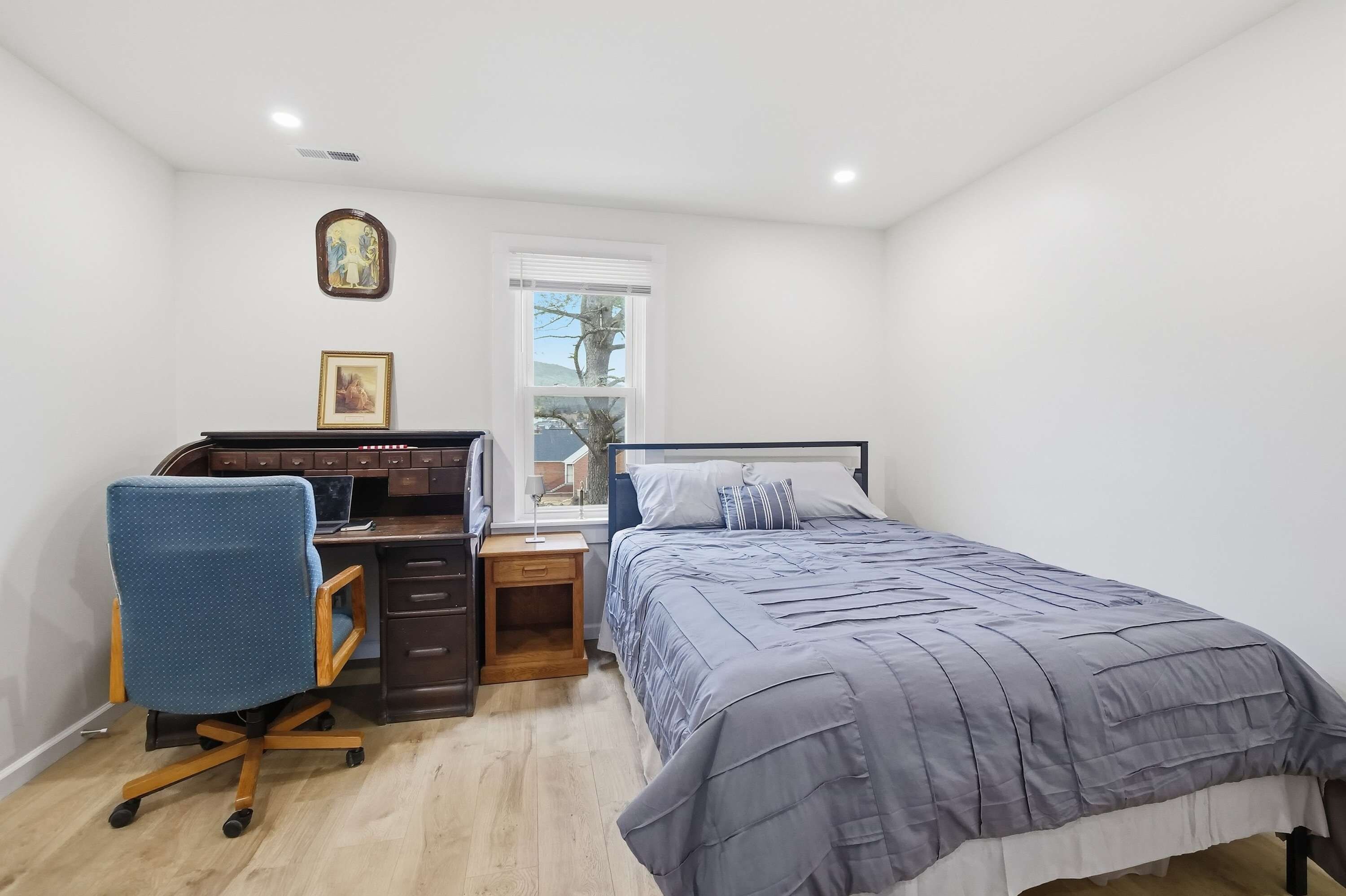 Quarto com cama, escrivaninha, cadeira e janela.