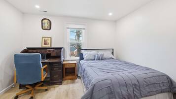 Quarto com cama, escrivaninha, cadeira e janela.