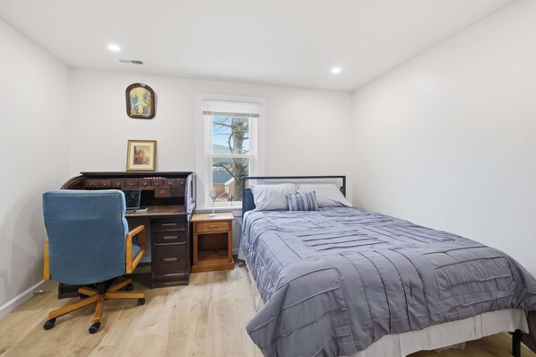 Un dormitorio con cama, escritorio, silla y ventana.
