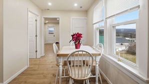 Uma área de jantar com mesa e cadeiras, janela com vista e corredor que leva a outro quarto.