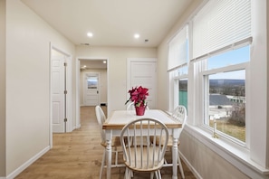 A dining area with a table and chairs, a window with a view, and a hallway leading to another room. - Historic Wardensville Home w Mountain Views (Wardensville)