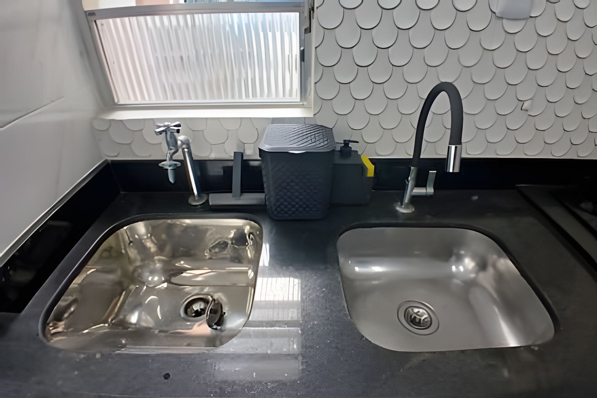 A kitchen with two stainless steel sinks, a window with blinds, and a decorative wall with a scalloped pattern.