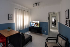 A living room with a TV, a black sofa, a wooden table, and a red chair. - SHB - Aconchego a Passos do Mar (Santos)