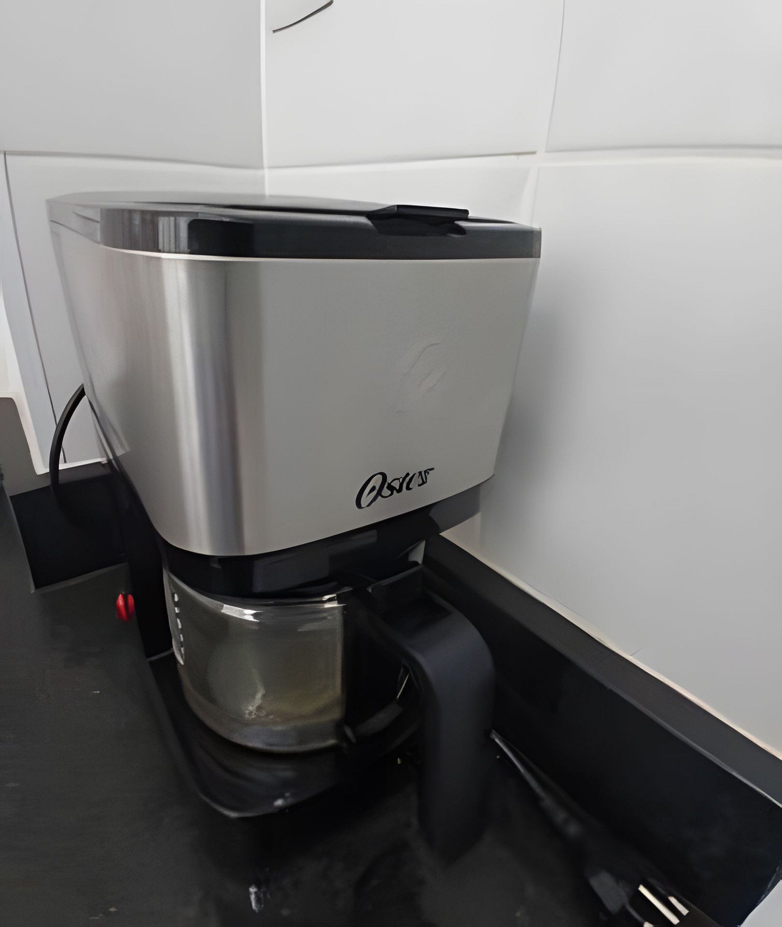 Een koffiezetapparaat met een transparante waterreservoir en een zwart opvangbakje.