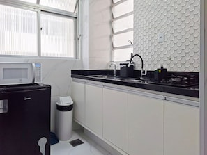 A modern kitchen with a microwave, sink, and stove. - SHB - Aconchego a Passos do Mar (Santos)
