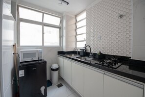 Una cocina compacta con microondas sobre un refrigerador pequeño, un lavamanos y una estufa.