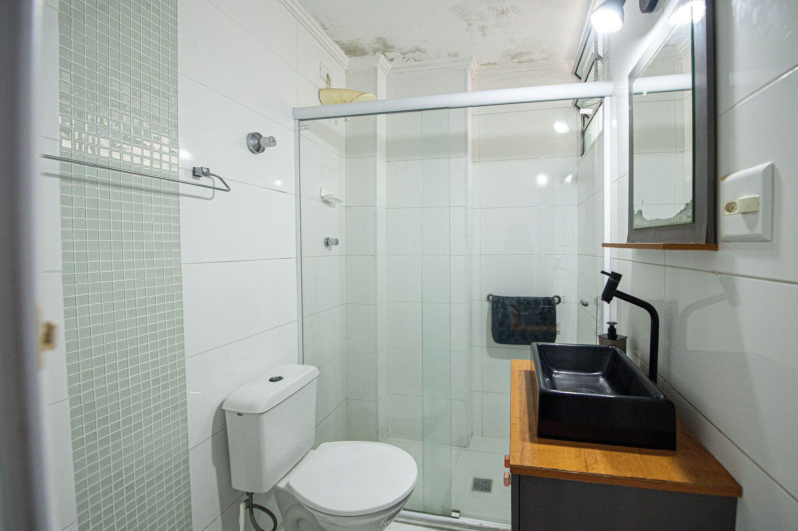 A small bathroom with a toilet, a glass-enclosed shower, and a sink with a mirror above it.