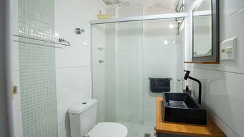 A small bathroom with a toilet, a glass-enclosed shower, and a sink with a mirror above it.