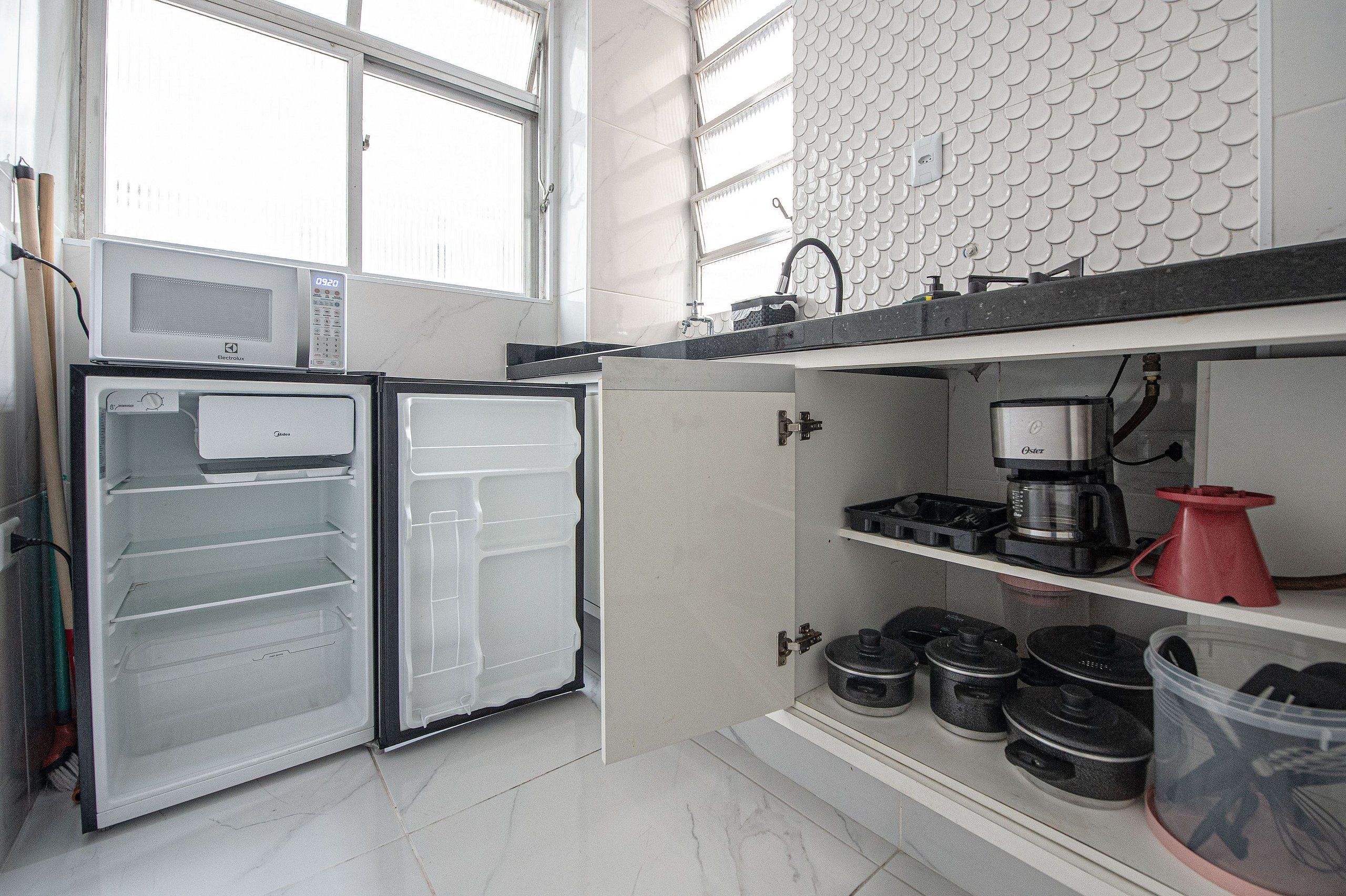 Una cocina equipada con microondas, refrigerador, cafetera y diversos utensilios.