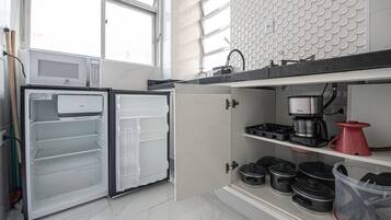 Una cocina equipada con microondas, refrigerador, cafetera y diversos utensilios.