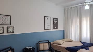 A bedroom with a bed, a chair, a small table, and a wall with framed pictures.