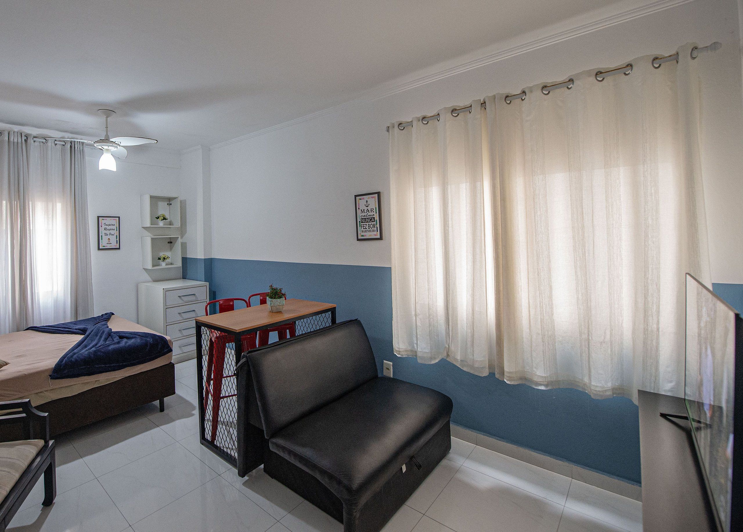 A room with a bed, a desk, a chair, a small table with a plant, and a TV.