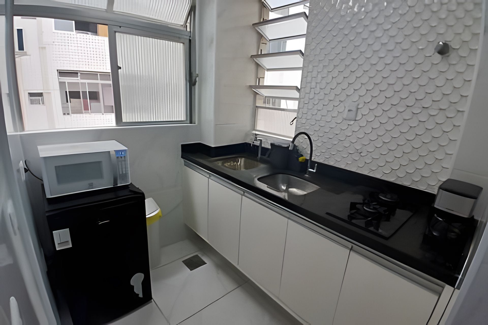 A modern kitchen with a black countertop, stainless steel sink, and a microwave.