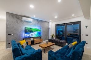 Ein modernes Wohnzimmer mit einem großen Flachbildfernseher, blauen Sofas, einem Holztisch und einer grauen Akzentwand.
