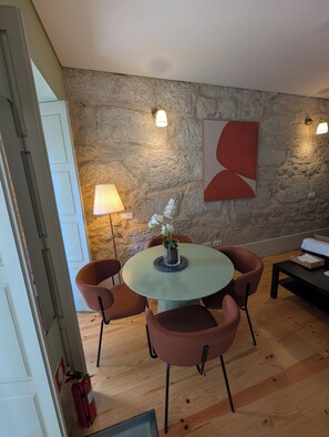 Ein Essbereich mit einem runden Tisch, vier Stühlen, einer Blumenvase, einer Lampe und einer Wand mit Steinoptik und abstrakter Kunst.
