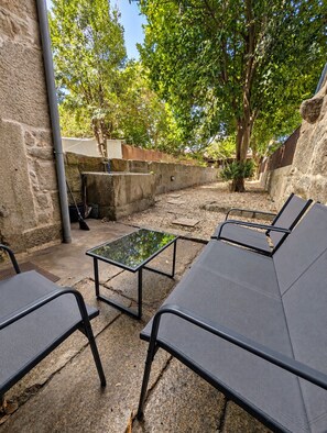 An outdoor seating area with a stone wall, a metal table, and lounge chairs. - Charming Porto House with Private Garden on Time Out's Coolest Street (Porto)