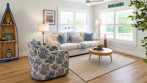 A living room with a sofa, a blue patterned chair, a coffee table, and a bookshelf. - The McKenzie House (Punta Gorda)