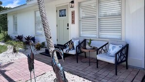 A white building with a covered porch, a door, and a window with blinds. - The McKenzie House (Punta Gorda)