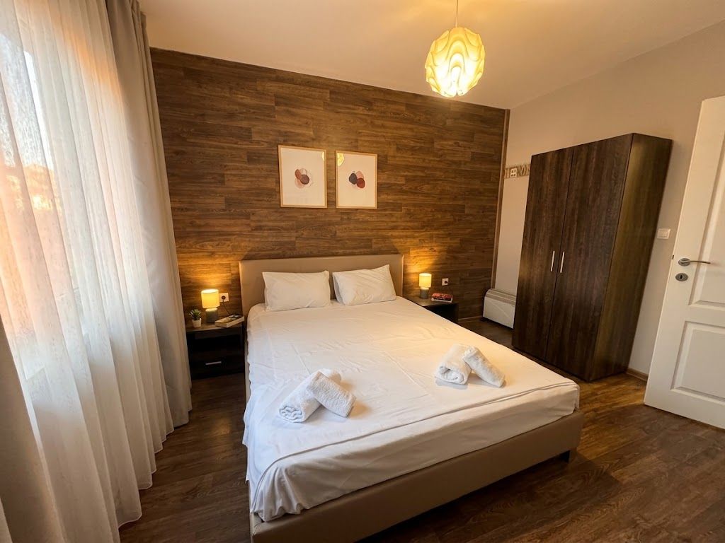 A hotel room with a large bed, wooden headboard, two bedside lamps, a wardrobe, and a door.